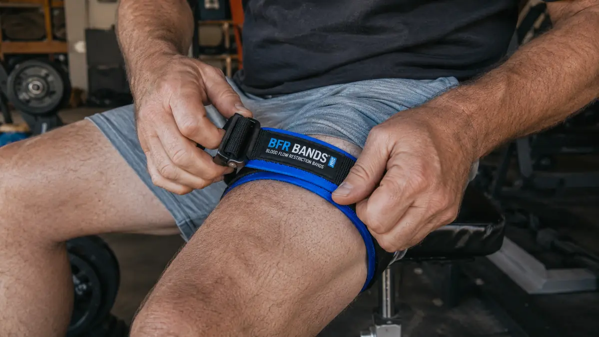 Close-up of BFR occlusion bands being wrapped around a man's upper thigh before a light leg workout