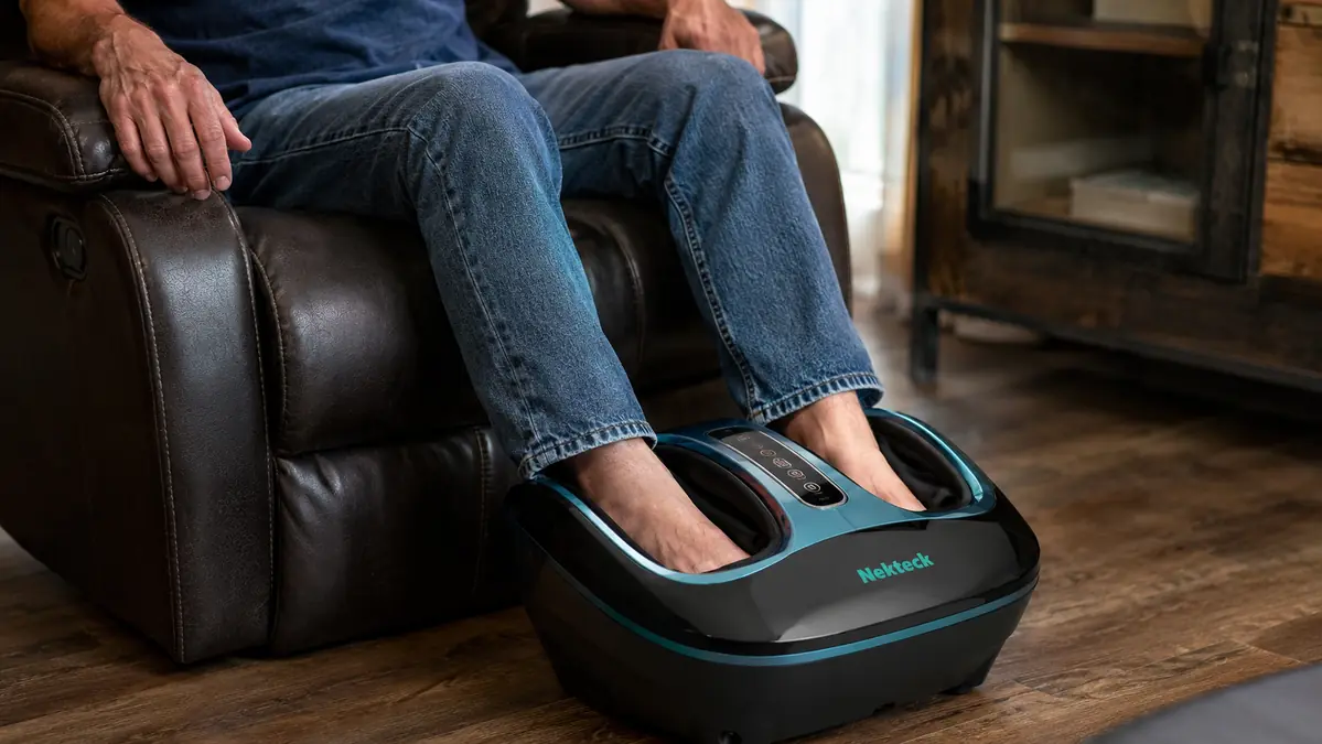 Close-up of bare feet resting inside an electric shiatsu foot massager with heat, remote control visible on the armrest