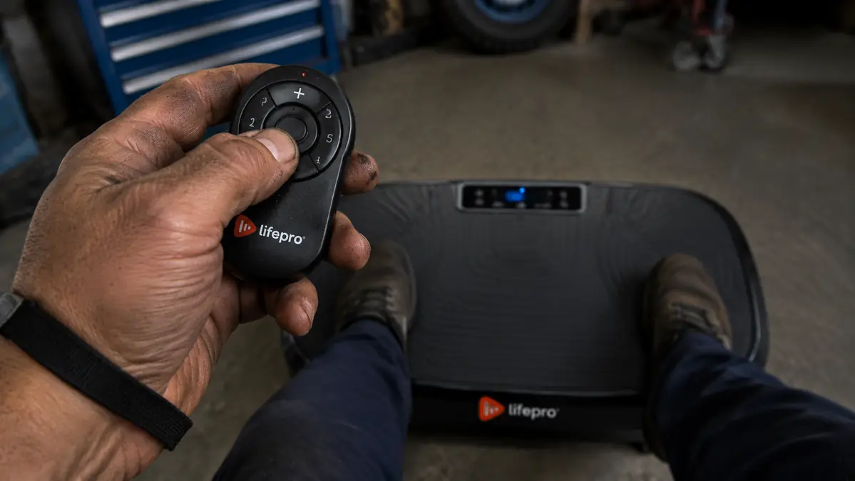 Close-up of a hand adjusting the speed dial on the vibration plate's wrist remote control